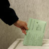 A woman drops her ballot in a voter box .