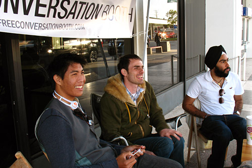 
                    Simmons sits next to Gino (left), another contributor and a high school senior who likes using his interactions at the booth to practice talking to girls. Avneet (right) is a college student at nearby California State University, Long Beach.
                                            (Ekene Okobi)
                                        