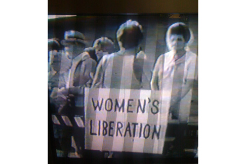 
                    A still of the film "Up Against the Wall Miss America," a short documentary of the 1968 Miss America protest.  The woman wearing the sign is Kathie Sarachild (Amatniek).
                                            (Ann Heppermann)
                                        