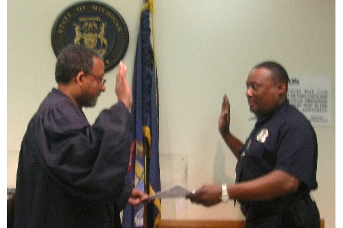 
                    Every sixth weekend, Magistrate Charles W. Anderson III presides over arraignments in Detroit's 36th District Court. On a recent weekend, he swears in Officer Alvis Owen, who's been in the Court Liaison Unit for the past eight years.
                                            (Desiree Cooper)
                                        