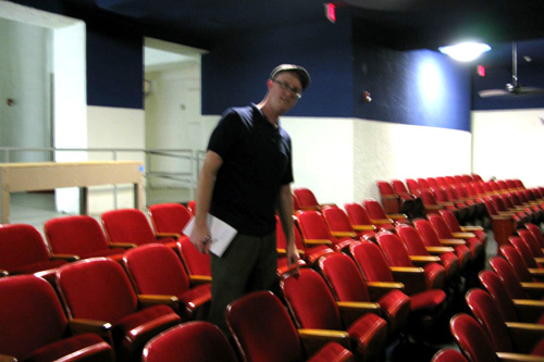 
                    Jason Roberts standing by the chair where Lee Harvey Oswald sat in the Texas Theatre in Oak Cliff. Oswald slipped into the theater after shooting Dallas Police officer J.D. Tippit. The Audie Murphy movie, "War Is Hell" was showing, but Oswald didn't stop to buy a ticket.
                                            (Julia Barton)
                                        