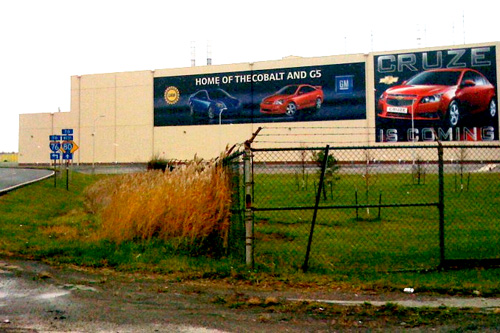 
                    This is the paint facility, only a portion of the massive Lordstown GM Assembly plant. The poster on the right says "Cruze is coming." The Chevy Cruze is a 5-passenger mid-size vehicle that will get 45 miles to the gallon and is seen as this plant, and this region's, potential lifesaver.
                                            (Krissy Clark)
                                        
