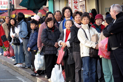 
                    People waiting for a bus on a busy Chinatown street watch the funeral procession passing by.
                                            (Julie Caine)
                                        