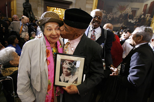 
                    Holding a photograph of himself as a 19-year-old pilot, Tuskegee Airmen Lt. Col. John Mulzac of Brooklyn, N.Y, kisses his wife Beatrice Mulzac after a ceremony honoring the World War II in Washington, DC.
                                            (Chip Somodevilla/Getty Images)
                                        