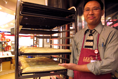 
                    Noel Santos, manager at Lee's in Irvine, with a tray of fresh baguettes.
                                            (Corey Takahashi)
                                        