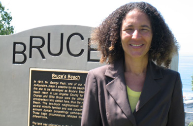 
                    Historian Allison Jefferson in front of the new plaque honoring the Bruce family, who used to own this stretch of seashore.  The Bruce's were early African-American settlers of Manhattan Beach.  They ran a seaside resort that was one of the few places where African-Americans could enjoy the beach.
                                            (Krissy Clark)
                                        