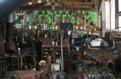 
                    Bobby's blacksmith shop.  He built it himself out of old tires, recylced wood and bottles for the windows.  To the right, you can see the speaker where he rigged up a record player to blast opera music.
                                            (Ann Heppermann)
                                        