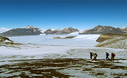 
                    Geologists hike to a dig site with Taylor Glacier in the background.
                                            (Courtesy Dry Valleys Productions)
                                        