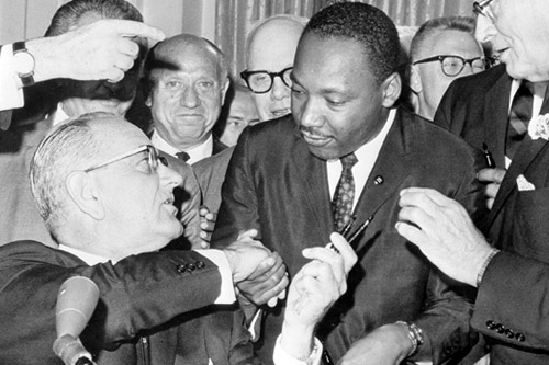 
                    President Lyndon Johnson (seated) shakes hands with Dr. Martin Luther King, Jr. in July of 1964 during the ceremonies for the signing of the civil rights bill at the White House.
                                            (AFP/Getty Images)
                                        